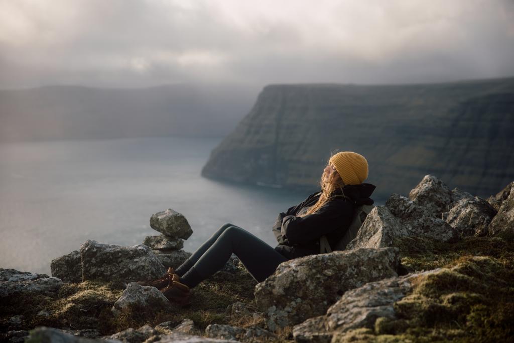 Girl, relaxing on a mountain. yellow beanie, hiking in nature on the Faroe Islands. 