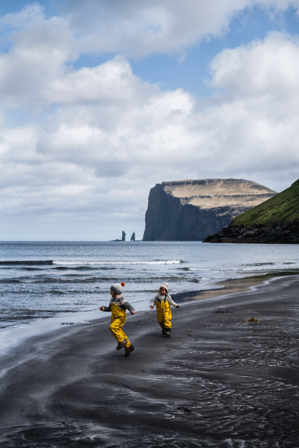 Children in yellow overalls playing on the sand beach of Tjornuvik, Tjørnuvík, Faroe Islands