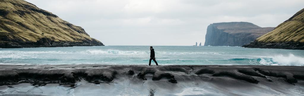 Man walking on the beach in Tjørnuvík, Faroe Islands. Scenic view of the sea, waves & rocks. Taken by Manuela Palmberger