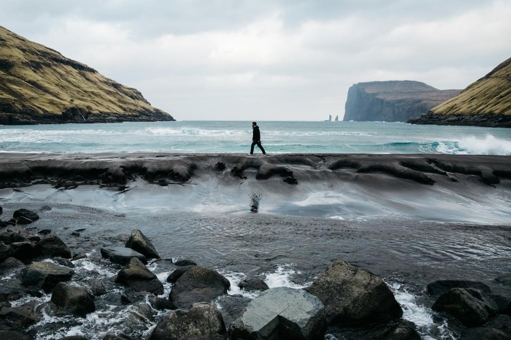 Man walking on the beach in Tjørnuvík, Faroe Islands. Scenic view of the sea, waves & rocks. Taken by Manuela Palmberger