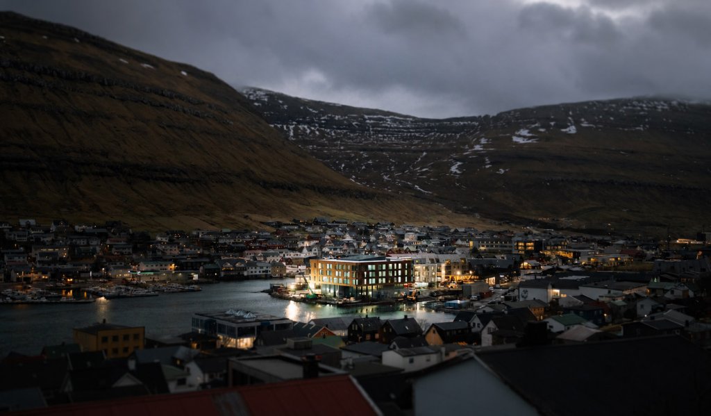 KG Hotel in Klaksvík surrounded by dramatic Faroese mountains and fjord. KG Hotel illuminated at dusk in the harbour of Klaksvík, Faroe Islands, surrounded by steep mountains, fjord views and Nordic coastal scenery