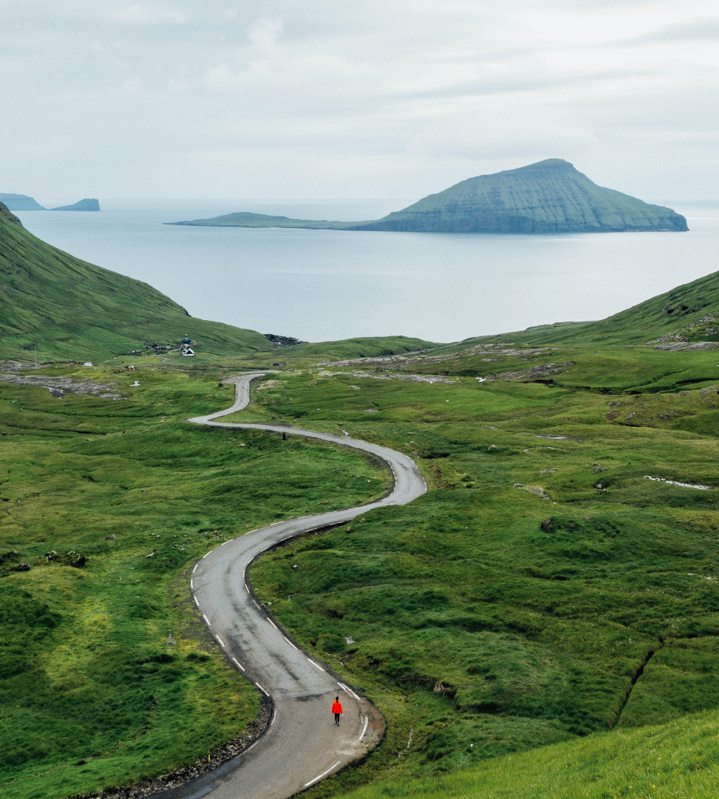 Man in red jacket, walking on a scenic road in Norðadalur, Faroe Islands. 